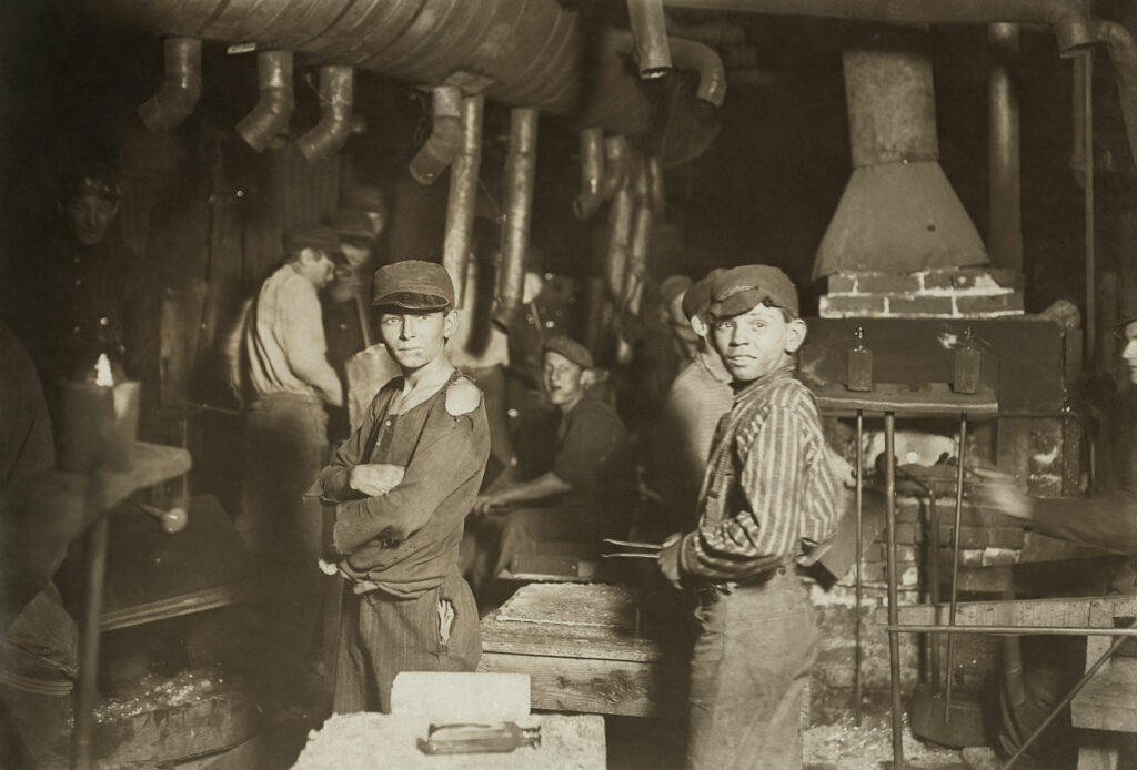 Drei Arbeiter posieren zwischen großen Rohren und industriellen Maschinen in einem dunklen Fabrikinneren.