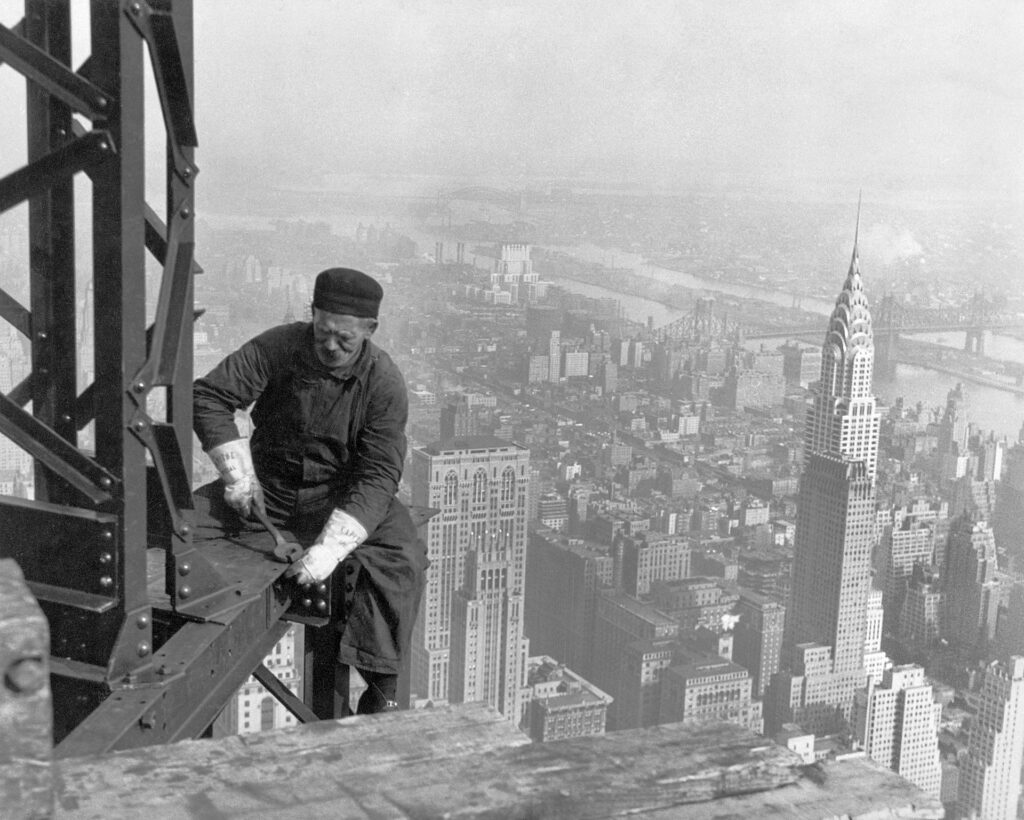 Ein Mann steht auf einem Metallgerüst und blickt über eine ausgedehnte Großstadt-Skyline mit vielen Wolkenkratzern.