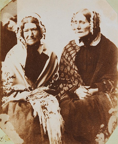 Zwei Frauen in historischer Kleidung sitzen zusammen für ein Porträtfoto.