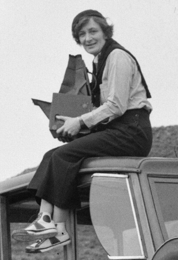 Eine Frau mit dunklem Haar sitzt auf einem Fahrzeug und hält mehrere braune Ordner.