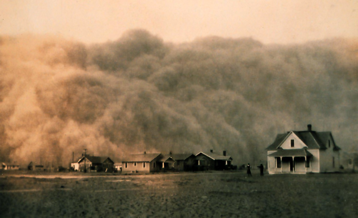 Mehrere hölzerne Gebäude stehen auf einem Feld und sind teilweise von dichtem Rauch oder Nebel verdeckt.