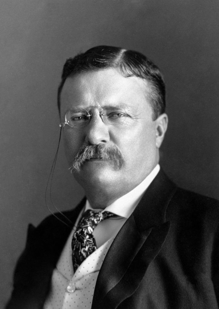 Schwarzweißporträt eines Mannes mit dunklen Haaren, einer Brille und einem Schnurrbart, der formelle Kleidung trägt.