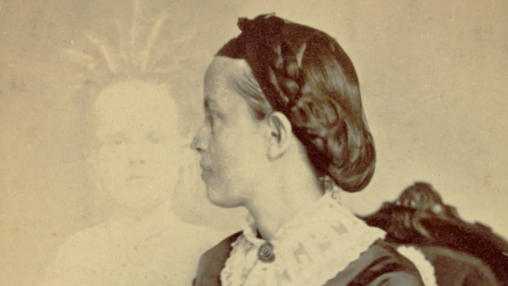 Porträt einer Frau im Profil mit dunkel gekämmtem Haar und einem gemusterten Kragen vor einem unscharfen Hintergrund.