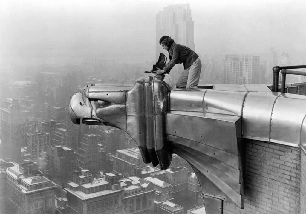 Ein Mann steht auf einer geschwungenen, metallischen Dachstruktur mit Blick auf eine nebelverhangene Großstadt.